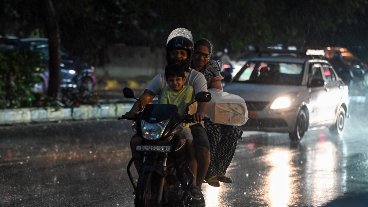 Commuters make their way through a glistening road during rainfall, in New…