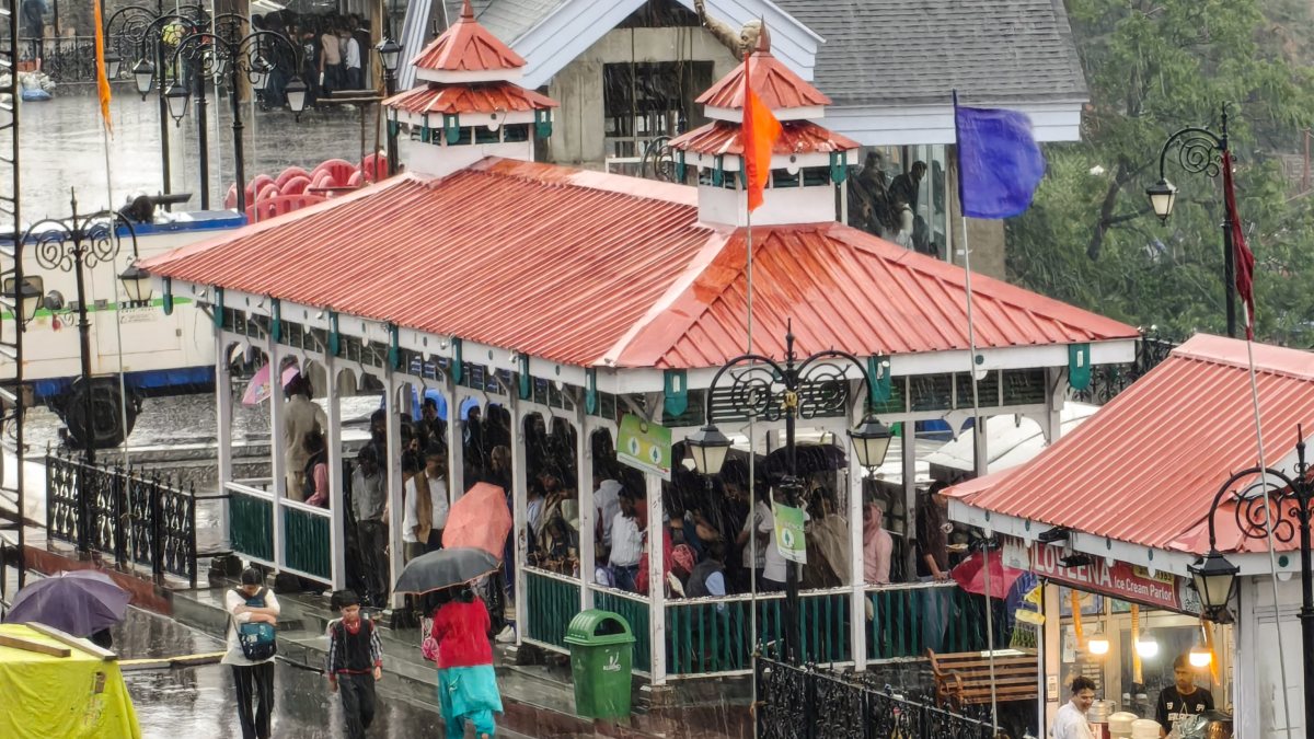 People stand under a shelter amid heavy rainfall, in Shimla on Thursday.