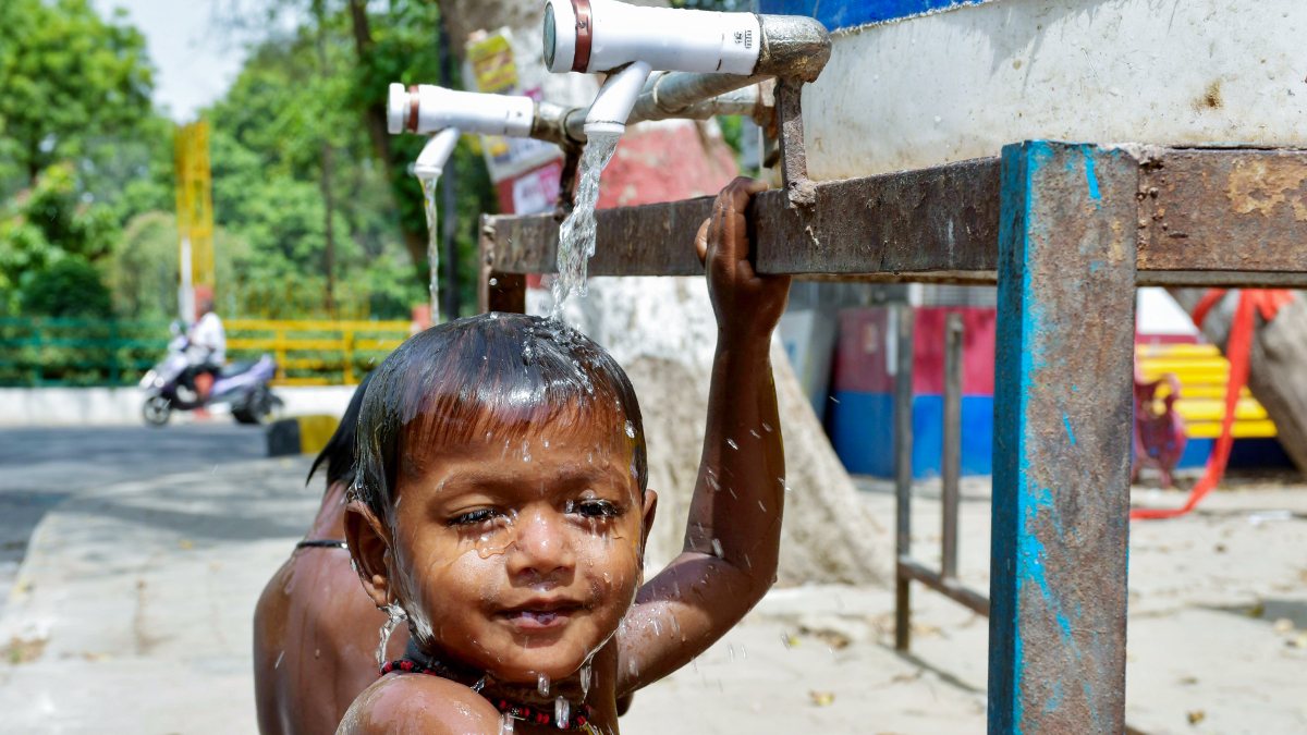 A child plays on the roadside in a water tap on a hot summer day, as seen, in…