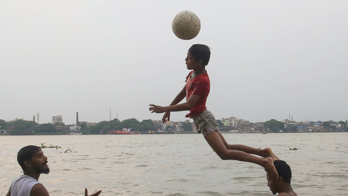 Boys play football in the waters of the River Ganges at Ahiritola Ghat while…