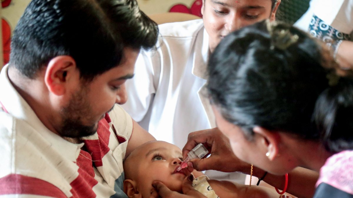 A health worker administers oral polio vaccine drops to a child during the…