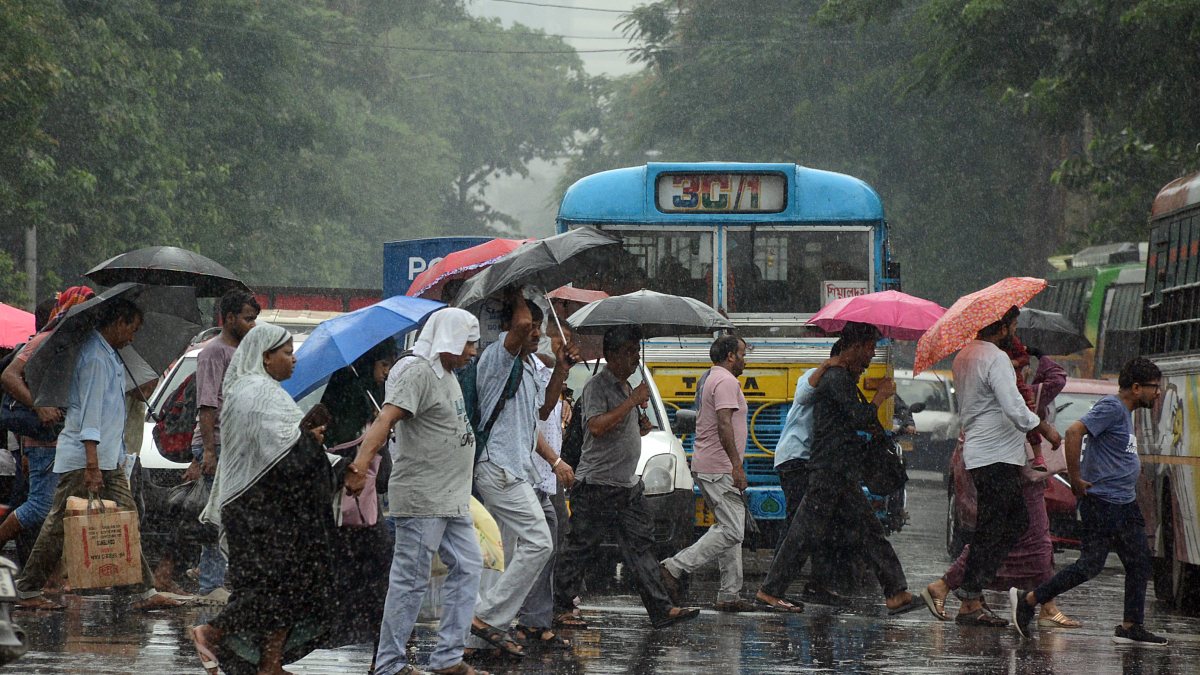 Pedestrians cross road holding umbrellas amid heavy rain in Kolkata