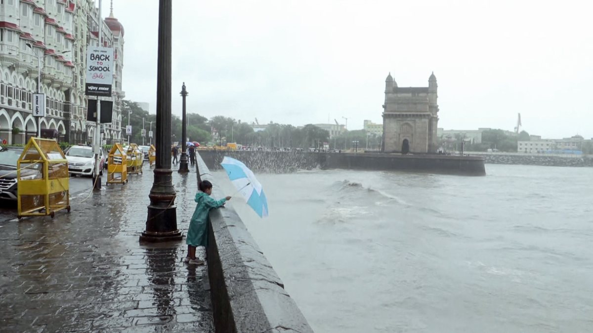A child wearing a raincoat and holding an umbrella stands on the promenade near…