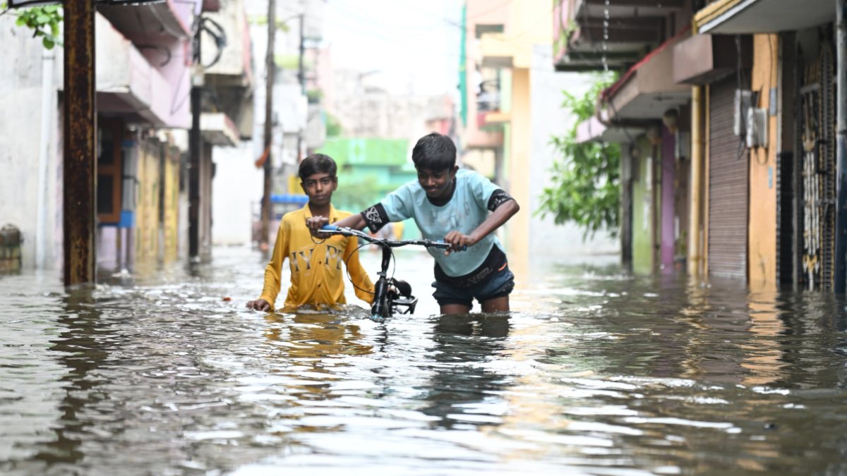 Two boys wade through waterlogged Raipur street with bicycle