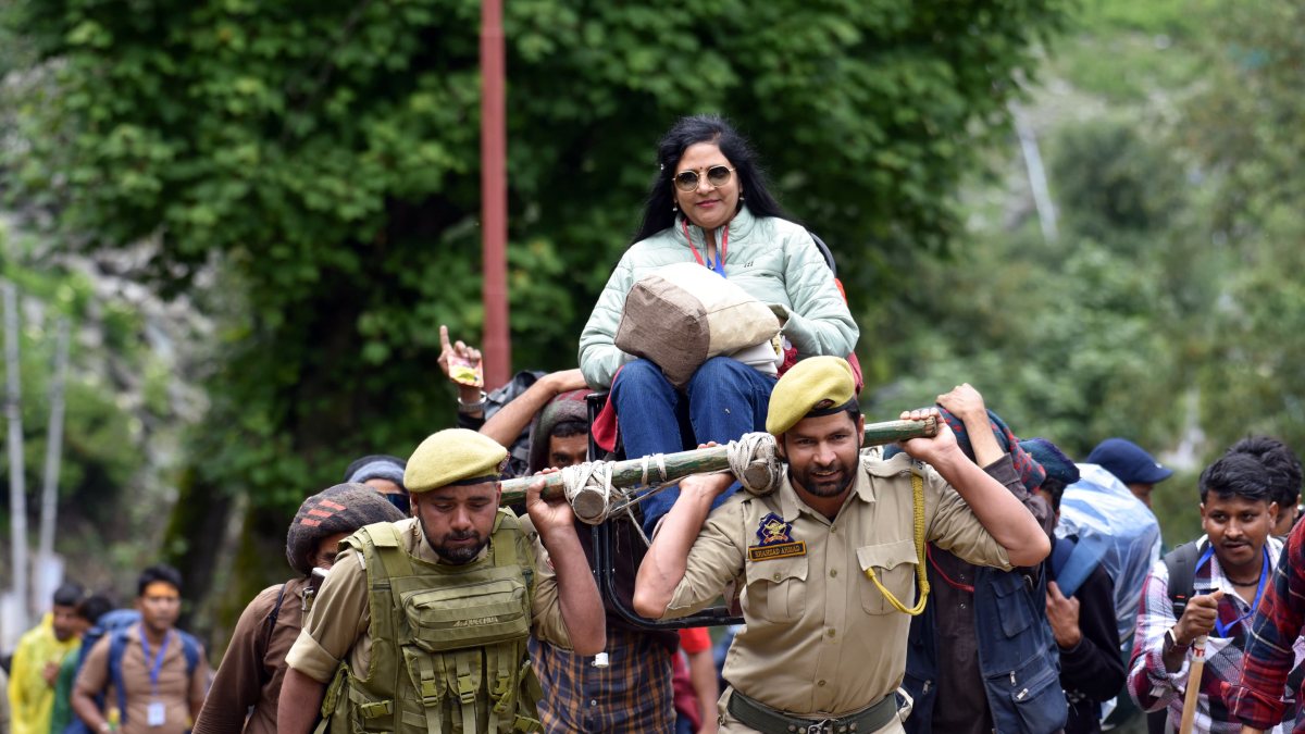 Security officials carry pilgrim on palanquin through mountain trail