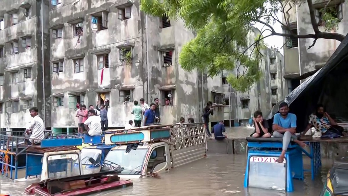 People sit on vehicles in waterlogged Surat road after heavy rain