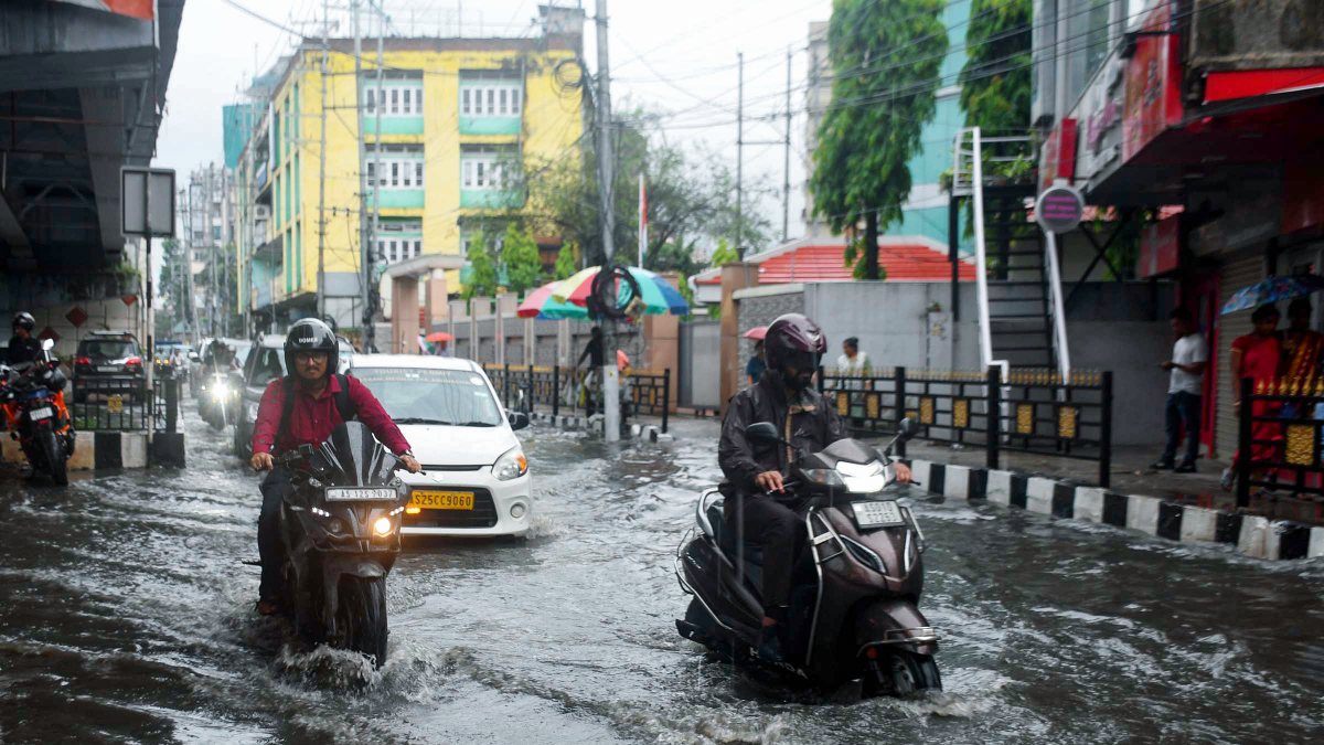 Commuters wade through waterlogged road after heavy rain in Guwahati