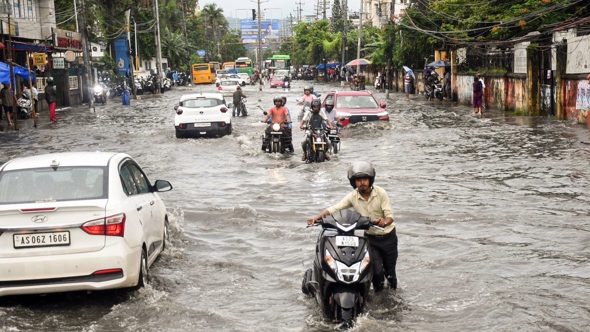 Commuters wade through waterlogged street after heavy rain in Guwahati