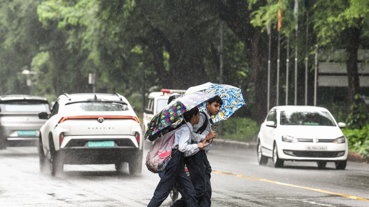Schoolchildren cross rain-soaked Akbar Road in New Delhi