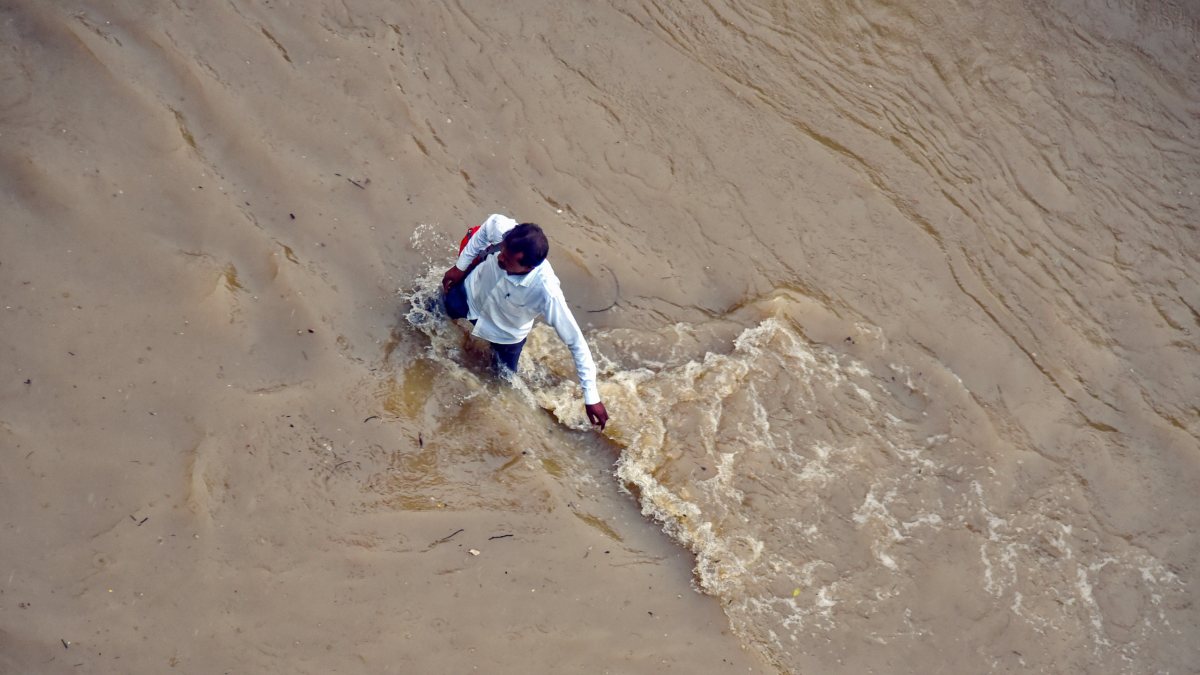 A man wades through the waterlogged road caused by continuous rainfall, in…