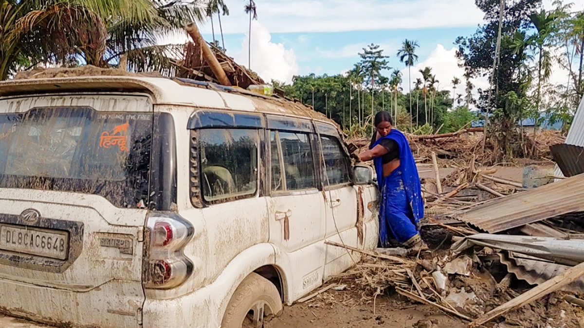 Woman stands near vehicle buried in mud after Dikhow River flood