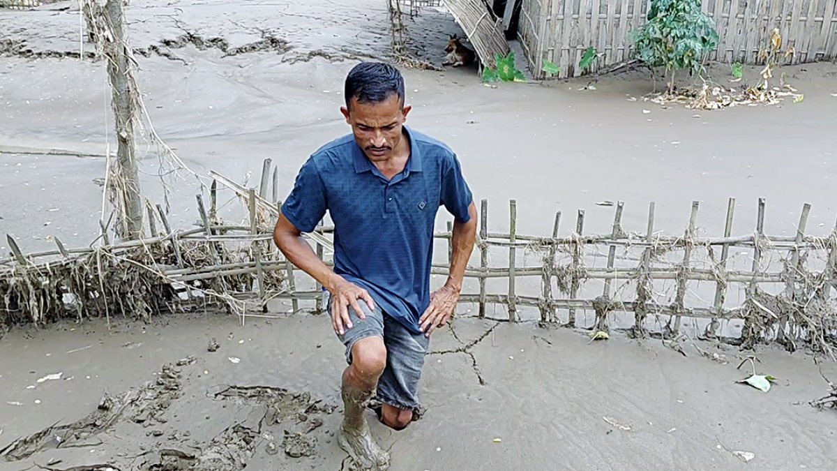 Man walks through thick mud after floodwaters recede in Assam