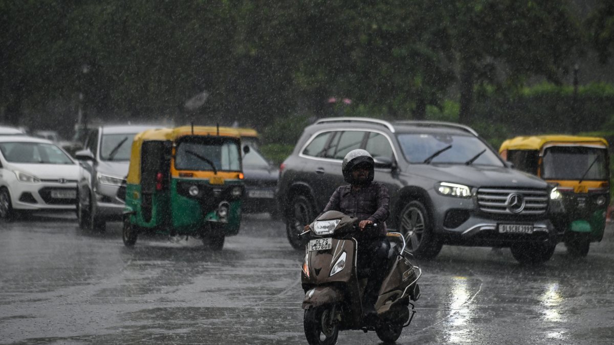 Commuters wade through a rain-slicked road amid heavy rainfall, in New Delhi on…