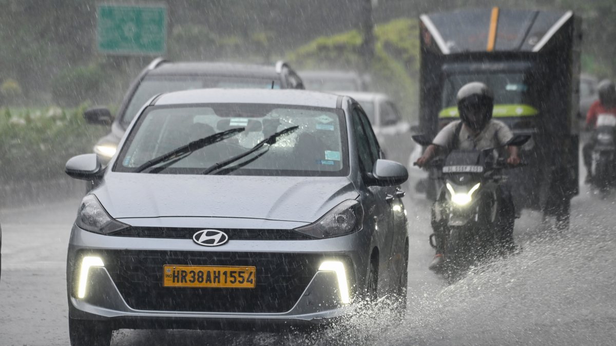 Commuters wade through a rain-slicked road amid heavy rainfall, in New Delhi on…
