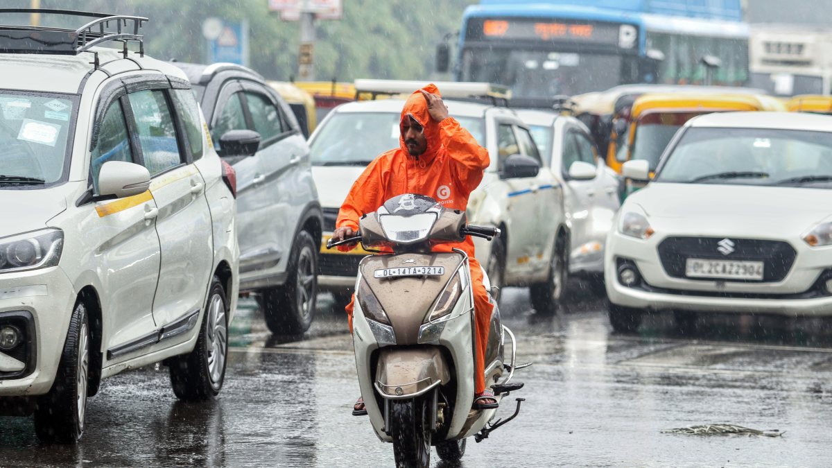 Delhi delivery rider waits out rain shower at signal
