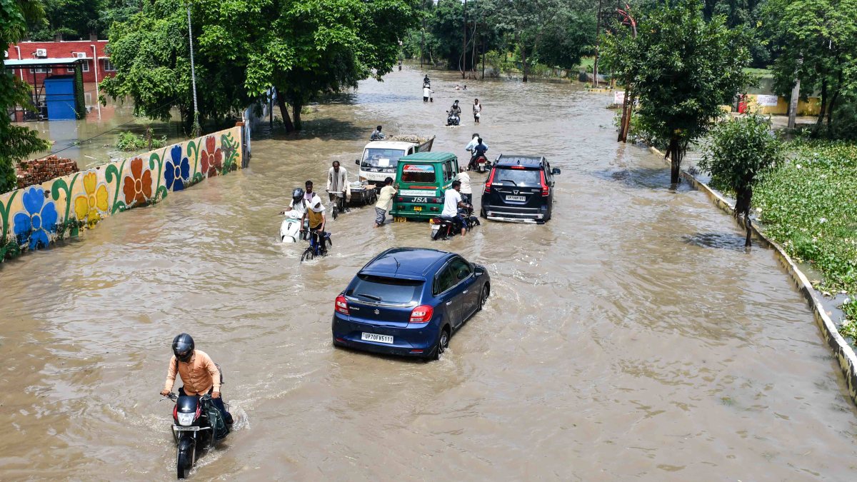 Commuters wade through waterlogged road after monsoon rain in Prayagraj