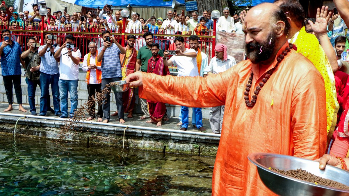 Head priest feeds fish at Martand Sun Temple in Pahalgam