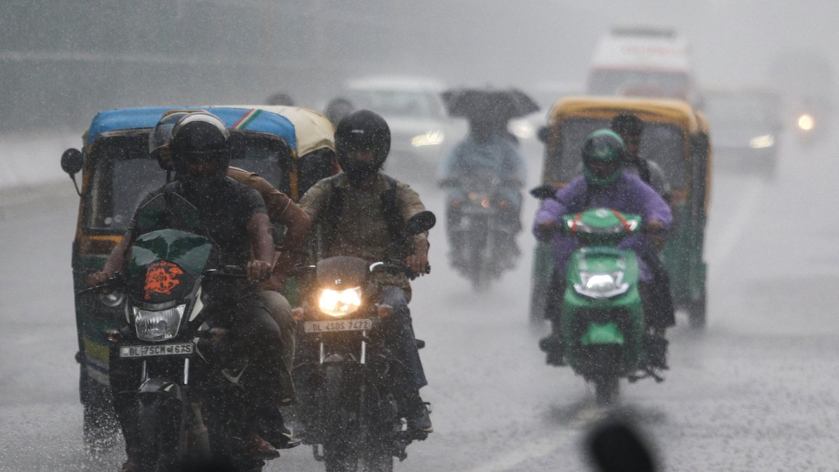 Commuters make their way through a rain-slicked road amid heavy rainfall, in…
