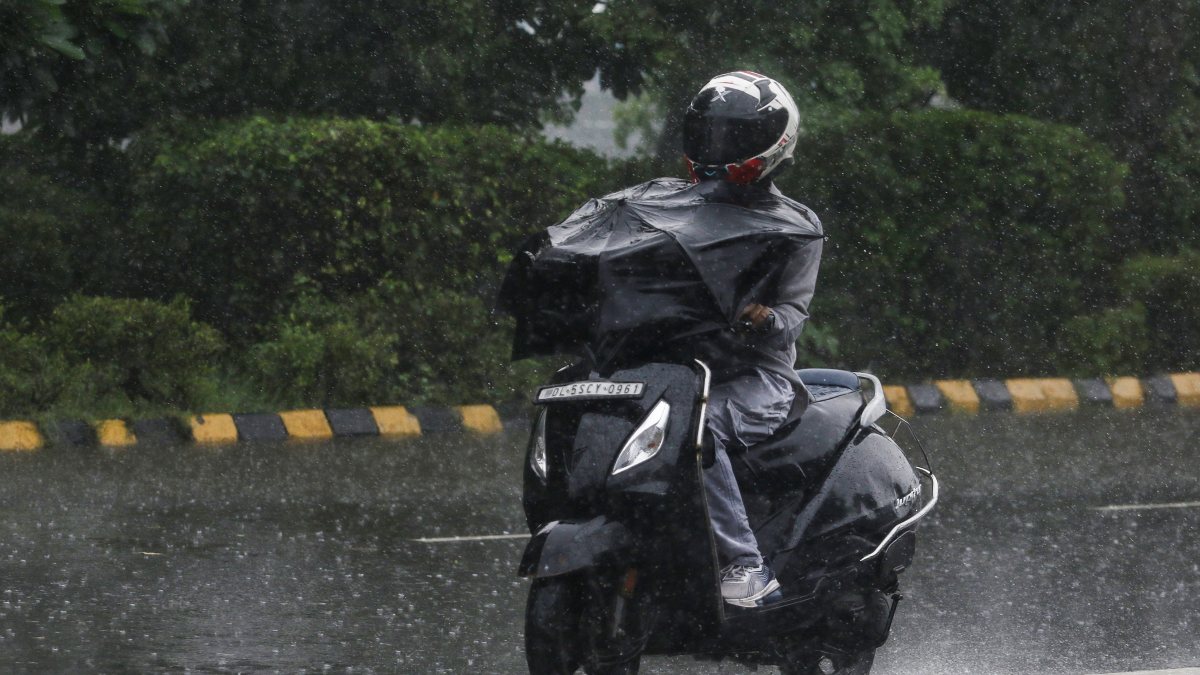 A commuter on a two-wheeler with an umbrella makes way through a rain-slicked…
