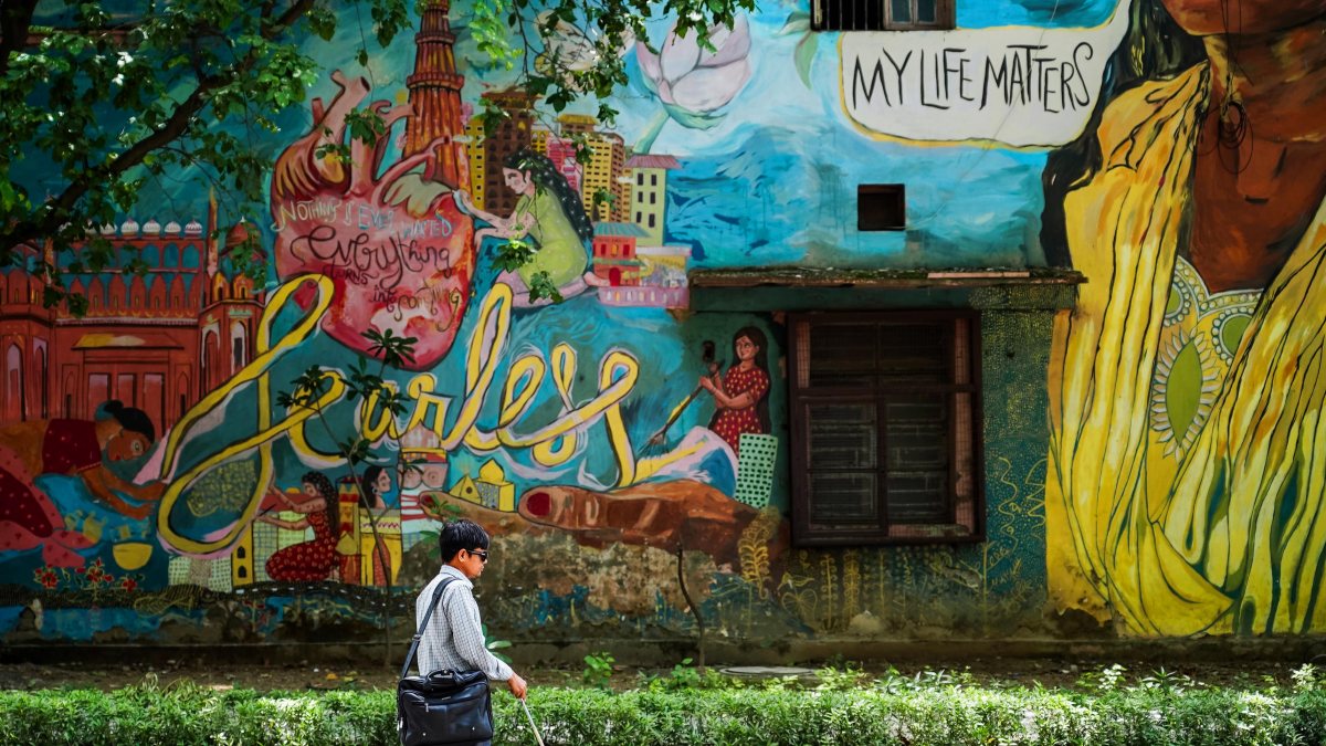 Visually impaired man walks past mural with 'Fearless' message in Delhi