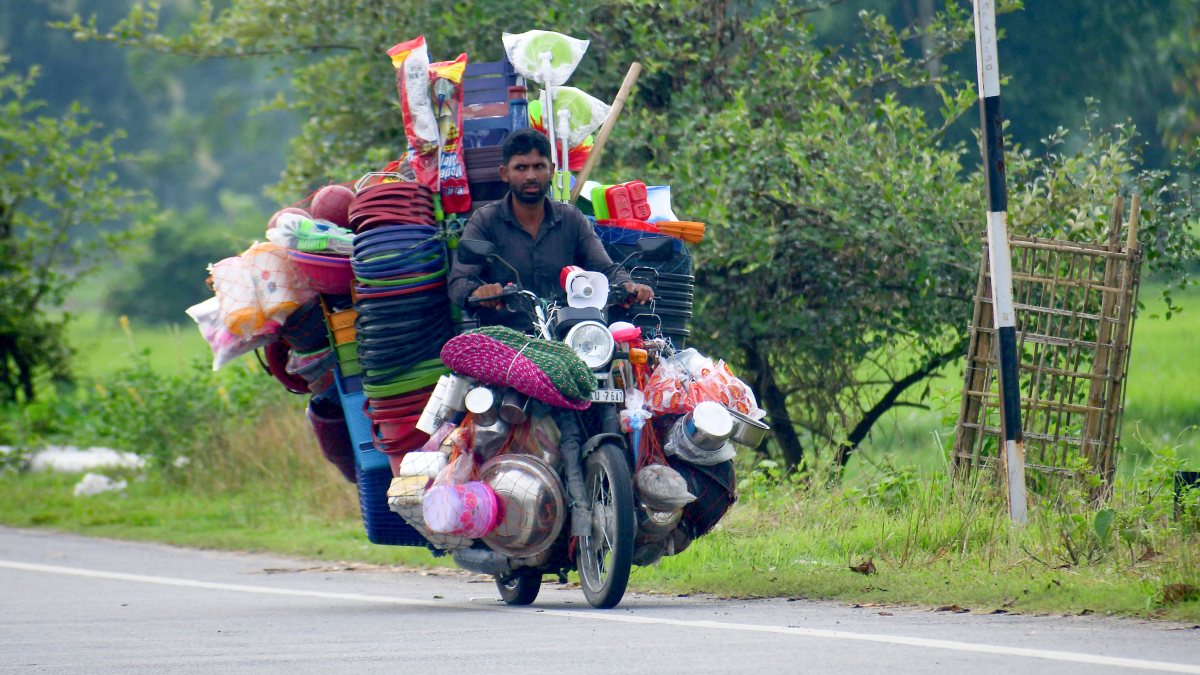 Vendor rides bike loaded with plasticware for sale in Nagaon