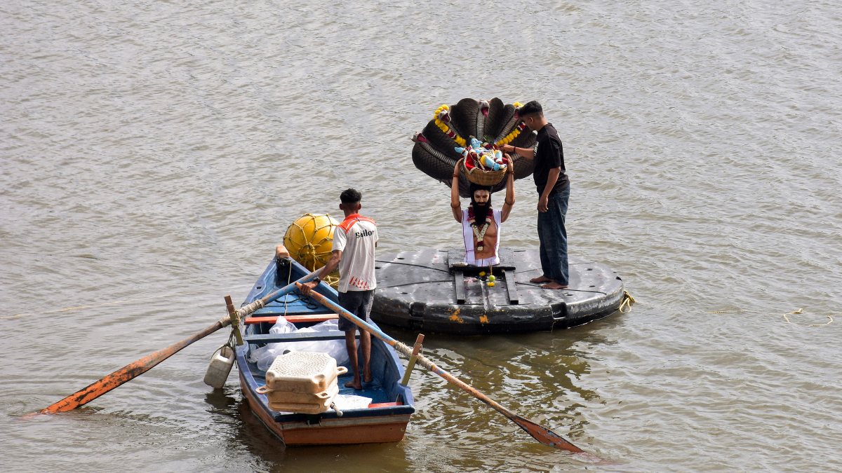 Man stands by Vasudeva statue as rowboat skims Tapi River in Surat