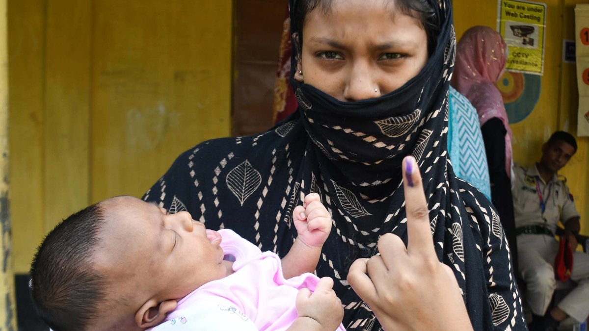 Woman with child shows inked finger after voting in Assam bypoll